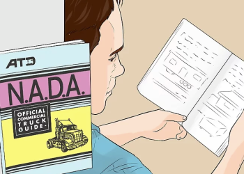 Person reading a mobile home valuation guide alongside the N.A.D.A. official commercial truck guide to estimate value.