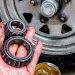 Mechanic holding greasy trailer wheel bearings beside a trailer hub during replacement and maintenance.