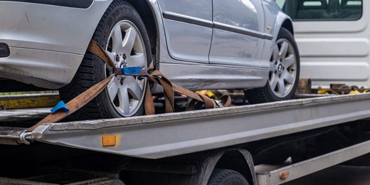 Car secured on a flatbed trailer using heavy-duty ratchet straps across all four wheels for safe transport.
