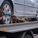 Car secured on a flatbed trailer using heavy-duty ratchet straps across all four wheels for safe transport.