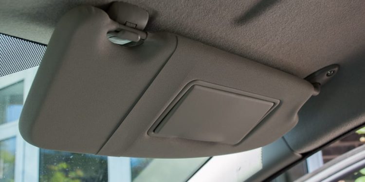 A close-up view of a car’s sun visor mounted above the windshield, showing the hinge and clip mechanism used for removal and replacement.